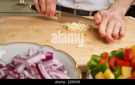 Man's hands cutting fresh garlic in the kitchen, preparing a mea Stock Photo