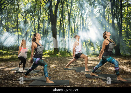 Group of youngsters keep in shape exercising in sunlight woods Stock Photo