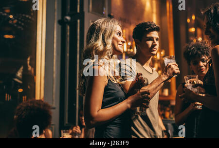 Group of people at party in pub at night. Young friends in nightclub enjoying drinks and chatting. Stock Photo