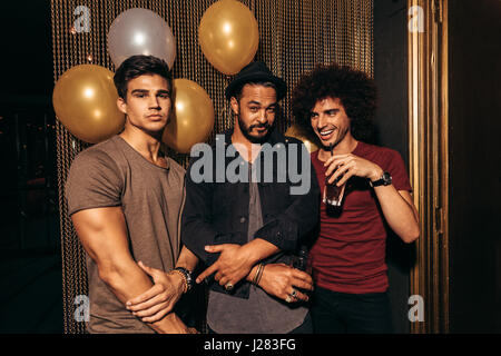 Portrait of three young men partying at the nightclub. Group of men having good times at pub.