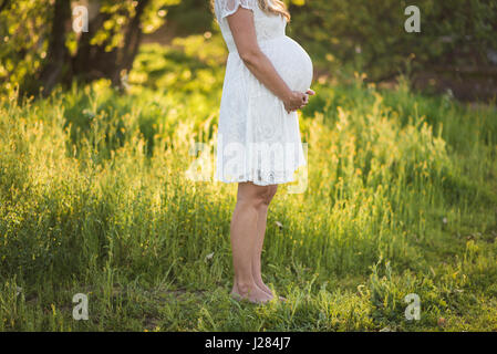 Low section of pregnant woman touching abdomen while standing on grassy field in park Stock Photo