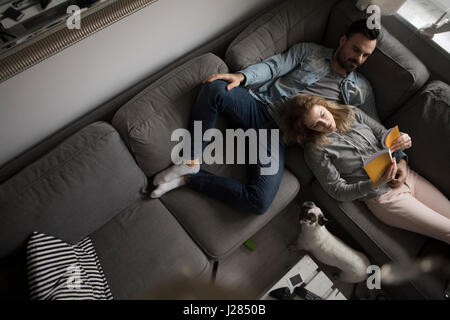 High angle view of couple reading book while relaxing on sofa by French bulldog at home Stock Photo
