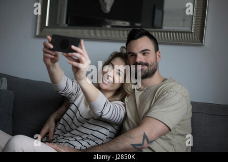 Happy couple taking selfie while sitting on sofa at home Stock Photo