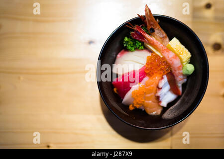 Chirashi sushi, Japanese food rice bowl with raw salmon sashimi, mixed seafood, top view, darken edge, copy space on wooden table, focus on salmon egg Stock Photo