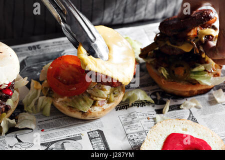 process of cooking hamburger. chef on the kitchen table making out the ingredients of the Burger. Beef Patty cooked on the coals. Vegetables and cheese and homemade sauces Stock Photo