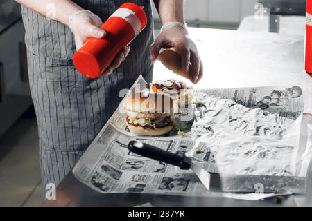 process of cooking hamburger. chef on the kitchen table making out the ingredients of the Burger. Beef Patty cooked on the coals. Vegetables and cheese and homemade sauces Stock Photo