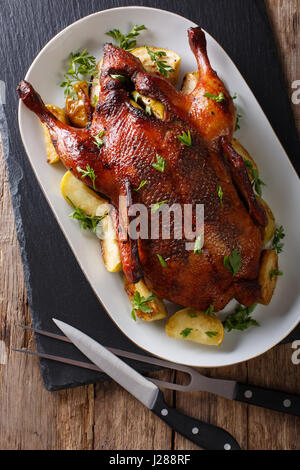 Delicious whole baked duck with apples close-up on a platter on the table. Vertical view from above Stock Photo