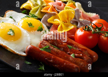 Delicious breakfast: fried egg, sausages, farfalle pasta and tomatoes close-up. Horizontal Stock Photo