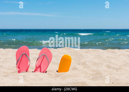 Sunscreen bottle and pink flip flops on the beach Stock Photo