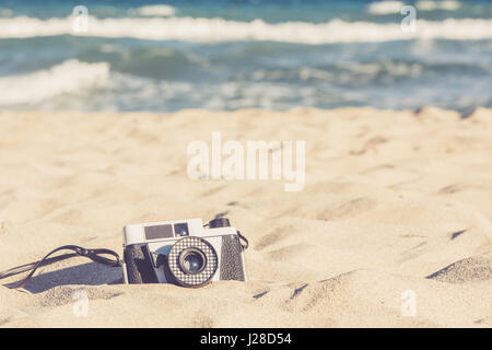 Old vintage camera lying in the sand on the beach Stock Photo
