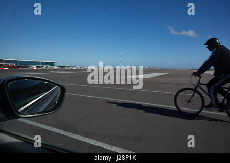 Gibraltar, airport, cars and a cyclist crosses the runway, which is crossed from the main road 'Winston-Churchill Avenue' Stock Photo