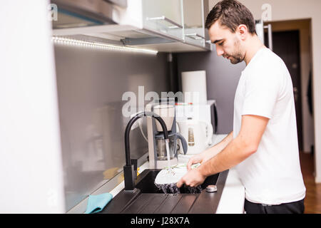young happy man doing the dishes smiling confident and relaxed enjoying doing domestic work Stock Photo