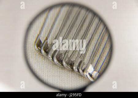 A few safety pin under a magnifier on a fabric background Stock Photo