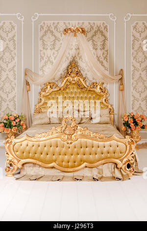 Luxury bedroom in light colors with golden furniture details. Big comfortable double royal bed in elegant classic interior Stock Photo