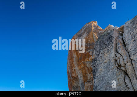 Detail of granite rock against blue sky with traces of red iron in surface weathered and with signs of erosion Stock Photo