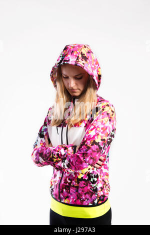 Attractive young fitness woman in colorful hooded sweatshirt, arms crossed. Studio shot on gray background. Stock Photo