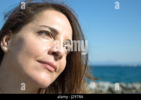 Portrait of a woman 45 years old, looking away, thinking, brown eyes, beach background. Stock Photo