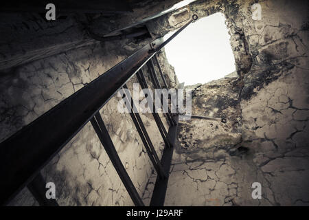 Old empty abandoned bunker interior with rusted metal ladder going up to glowing manhole Stock Photo