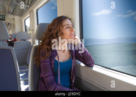 red hair woman dressed in purple and blue, sitting traveling by train pensive looking through the window Stock Photo