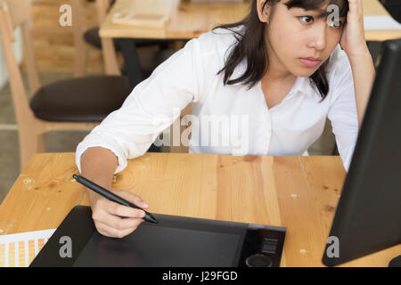 freelance graphic designer feeling exhausted, stressful and has headache, clasping head with hands at office with digital tablet and color swatch cata Stock Photo