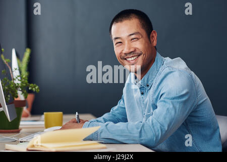 Smiling young Asian entrepreneur working at his office desk Stock Photo