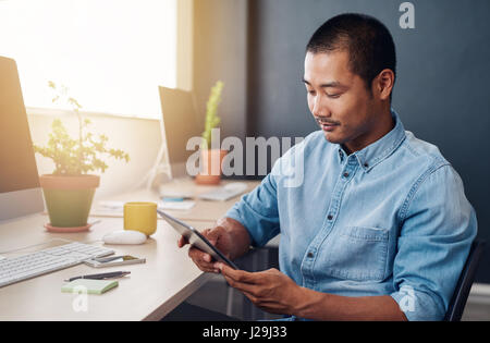 Focused Asian designer using a digital tablet at his desk Stock Photo