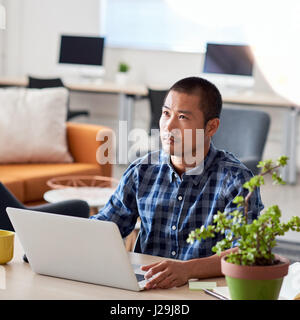 Young Asian architect deep in thought working in office Stock Photo