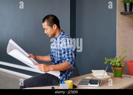 Focused young Asian architect reading blueprints in an office Stock Photo