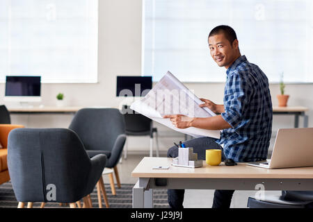 Confident Asian architect reading blueprints in an office Stock Photo