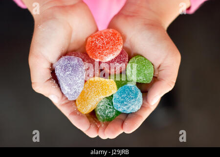 Child hands full of colorful jelly candies with sugar. Dark background Stock Photo
