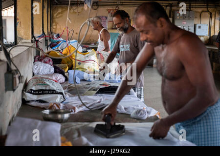 Three men work in the ironing of clothes in the municipal laundry of the city of Kochi Stock Photo