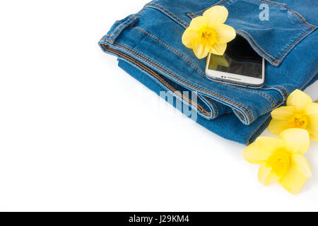 New blue denim jeans with a white cell phone, mobile phone, and yellow narcissus flowers in the back pocket on white background with lots of copy spac Stock Photo