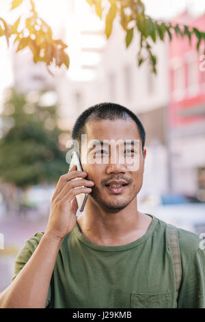 Young Asian man having a conversation on his cellphone outside Stock Photo