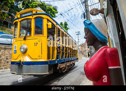 RIO DE JANEIRO - JANUARY 31, 2017: A brightly painted statue of a Brazilian woman stands on the street as a traditional tram passes in Santa Teresa. Stock Photo