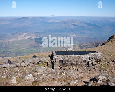 Hikers outside the summit shelter on Cadair Idris. The view is to the north, over the Rhinog mountains to a distant Snowdon Stock Photo