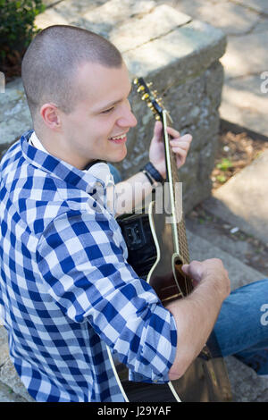 Handsome young man enjoying the park, sitting and playing guitar. Selective focus and small depth of field. Stock Photo