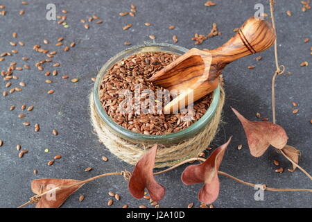 A glass bowl of flax seeds with olive scoop surrounded by artificial flowers on a grey abstract background. Healthy eating concept. Stock Photo