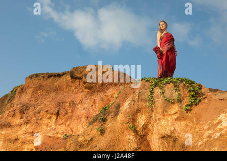 Young woman dressed in a red silk sari standing on a tropical paradise beach in Mirissa, Sri Lanka. Stock Photo