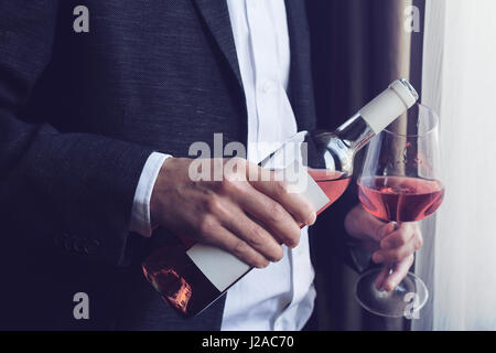 Horizontal close up of Caucasian man in black suit and white shirt pouring rose wine into a tall glass from a bottle in a bar by the window natural li Stock Photo