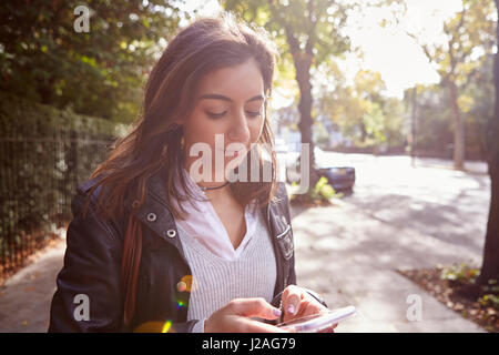 Young woman standing in street using mobile phone, back lit close up Stock Photo
