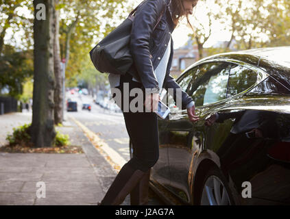 Young woman holding phone getting into the back of a car Stock Photo