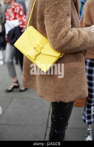 LONDON - FEBRUARY, 2017: Mid section of woman standing in street wearing short brown coat and yellow Christopher Kane handbag during London Fashion Week, vertical Stock Photo