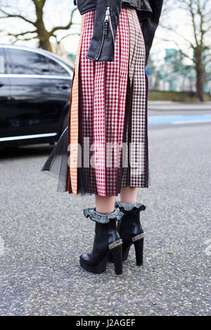LONDON - FEBRUARY, 2017: Low section of woman wearing high heeled ankle boots and pleated skirt at roadside during London Fashion Week, vertical, back view Stock Photo