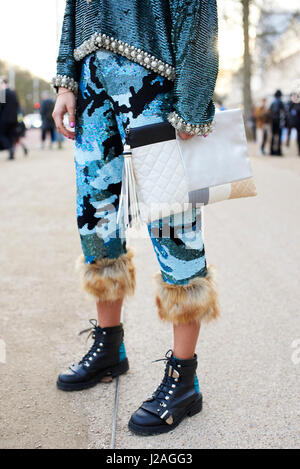 LONDON - FEBRUARY, 2017: Low section of woman in Ashish trousers and top holding an oversized Chanel clutch handbag standing in the street during London Fashion Week, vertical, front view Stock Photo