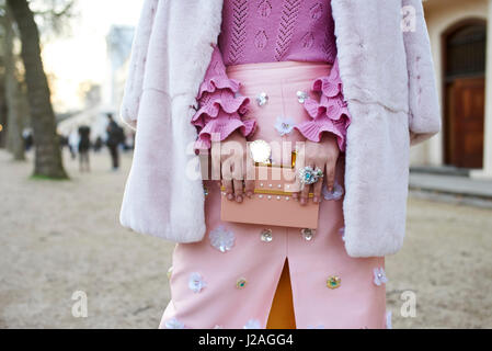 LONDON - FEBRUARY, 2017: Mid section of woman dressed in shades of pink, with a ruffle sleeved sweater, a coat over her shoulders and a skirt with appliqué, holding a decorated purse in the street during London Fashion Week, horizontal, front view Stock Photo