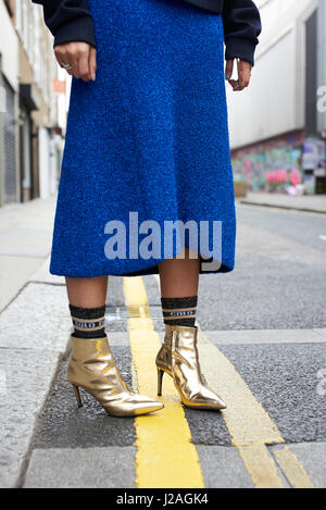 LONDON - FEBRUARY, 2017: Low section of woman wearing blue wool skirt, socks and gold ankle boots standing in the street during London Fashion Week, vertical Stock Photo