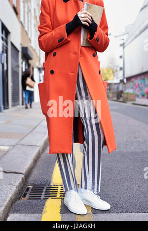 LONDON - FEBRUARY, 2017: Low section of woman wearing long orange coat and striped trousers standing in the street during London Fashion Week, vertical Stock Photo