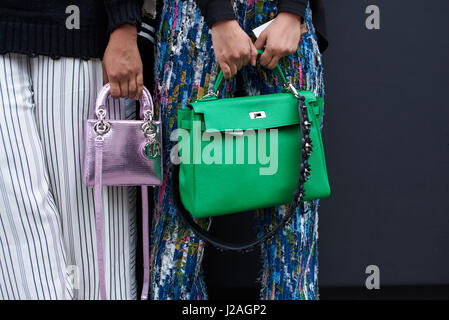 LONDON - FEBRUARY, 2017: Mid section of two women standing in a street holding designer handbags, a large green Hermes bag, and a small metallic Dior bag, during London Fashion Week, horizontal, front view Stock Photo