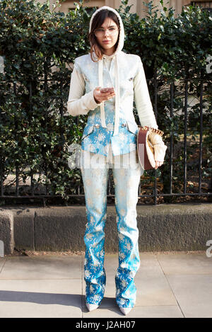 LONDON - FEBRUARY, 2017: Full length portrait of fashion model, stylist and blogger Doina Ciobanu wearing a blue and white patterned trouser suit with sleeveless jacket and white hoodie, holding a smartphone outside Pringle of Scotland show, London Fashio Stock Photo