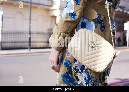LONDON - FEBRUARY, 2017: Mid section of woman wearing white Chanel cross body handbag and coat with floral decoration in street during London Fashion Week Stock Photo